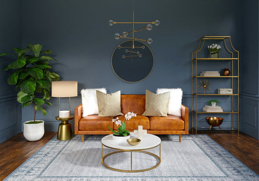 A modern living room with a leather sofa, gold chandelier, marble coffee table, table lamp, blue accent wall, and elegant decor.